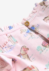 Tissu rose avec des bords froncés et un bouton en bois, illustré de chevaux portant un équipement d'équitation et de barrières.