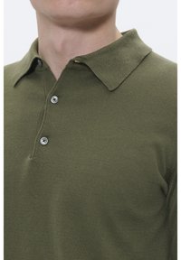 Polo verde oliva realizzata in tessuto a maglia liscia, con colletto a punta e tre bottoni argentati sulla patta.