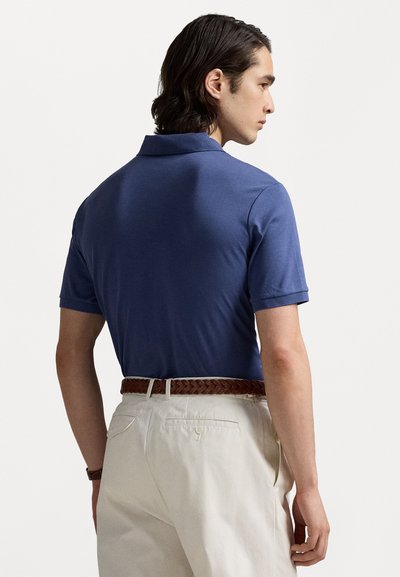 tricou polo albastru închis cu guler, mâneci scurte și un design ajustat, asociat cu pantaloni bej deschis, plisati și o curea împletită maro.