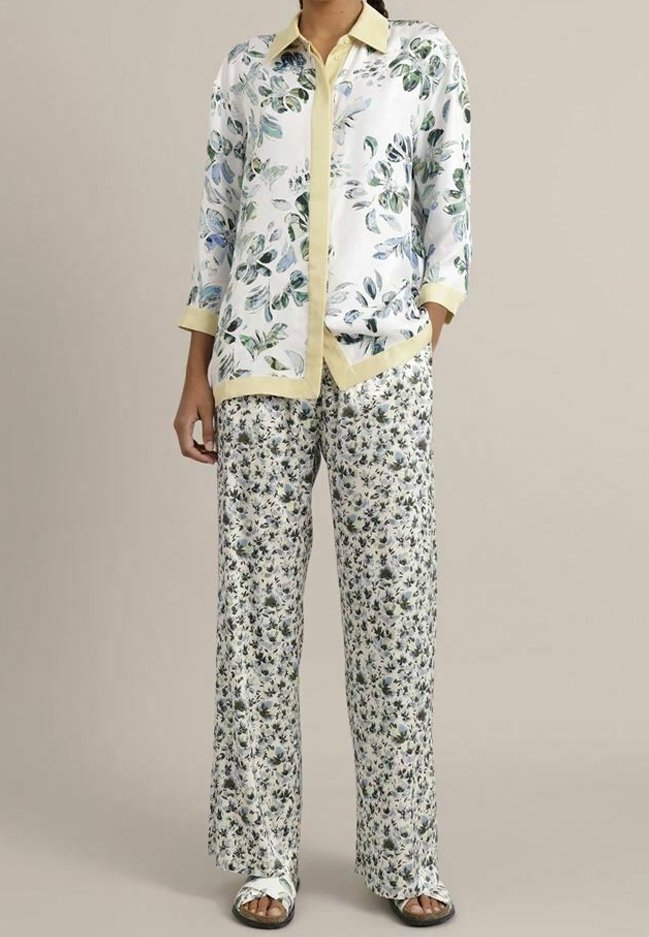 Personne portant une chemise blanche à motif floral avec bordure jaune et un pantalon ample à motif floral assorti ainsi que des sandales blanches.