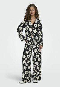 Schwarz gemustertes Zweiteiler-Outfit mit einem knöpfbaren, langärmeligen Oberteil und weitem Beinkleid; der Stoff hat eine strukturierte Optik.