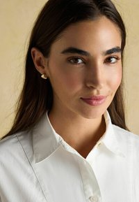 Weißes Hemd mit glatter Textur, featuring einen einzelnen goldenen Knopf als Akzent. Sanftes Licht betont den natürlichen Hautton.