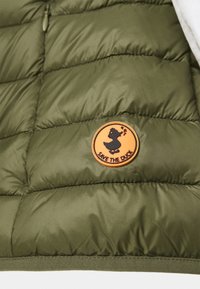 Olivgrön pufferväst med en horisontell quiltad design och en rund orange lapp med en svart ank-siluett som är märkt "SAVE THE DUCK."