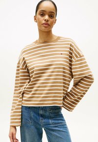 Brun og hvid stribet langærmet skjorte med rund hals, prydet med et lille logo på brystet. Sammen med blå denim jeans.