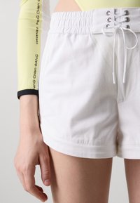Witte katoenen shorts met een elastische tailleband, voorzijde met vetersluiting en opgerolde mouwen. Close-up toont een gladde textuur en een strak ontwerp.