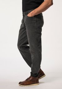 Mørkegrå jeans med en afslappet pasform, der har frontlommer og knaplukning. Båret med brune snørebåndsstøvler og sort skjorte.