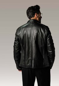 Veste de moto en cuir noir avec des détails côtelés sur les manches, finition texturée et coupe slim, portée avec un pantalon noir.