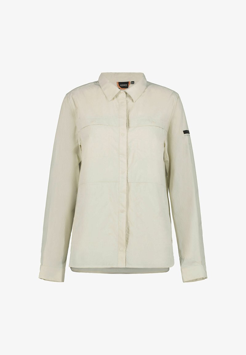 Chemise beige clair à boutons avec manches longues, deux poches poitrine et une texture subtile. Présente un logo de marque sur la manche gauche.