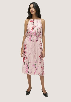 Gemustertes Midi-Kleid in Hellrosa mit roten und grünen Akzenten, Halsauschnitt und taillierter Taille; kombiniert mit schwarzen spitzen Absätzen.