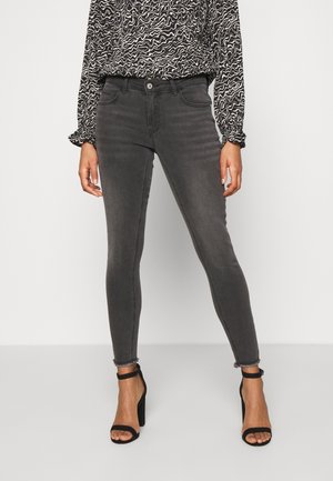 Woman wearing high-waisted faded black skinny jeans, black and white patterned blouse, and black high-heeled sandals.