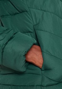 Giacca verde imbottita con design trapuntato, dalla morbida texture e tasca laterale integrata nella silhouette del capo.