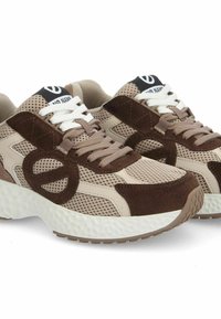 Des chaussures de sport beiges et brunes avec des matériaux en maille et en daim, dotées d'une semelle texturée, de lacets blancs et d'un logo sur la languette.
