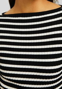 Top a righe bianco e nero con una texture a costine e una scollatura ampia e arrotondata. Le righe sono equidistanti, creando un motivo audace.