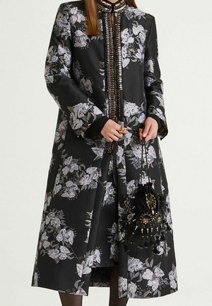 Long black floral coat with a textured fabric, featuring white and silver flowers, a high neckline, and a detailed front closure. Black bag with embellishments.
