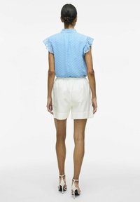 Lyseblå bluse med korte, flæset ærmer og prikker, parret med hvide shorts i mellemlængde med elastisk talje.