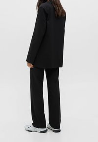 Black tailored blazer and matching pants, made of smooth fabric. The outfit features a relaxed fit and is paired with white sneakers.