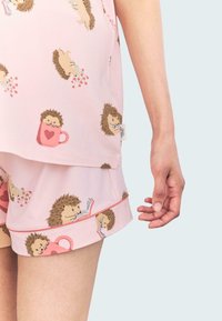 Conjunto de pijama rosa con patrones de erizos, de mangas cortas y pantalones cortos con un ribete rosa en contraste. Textura de tela suave.