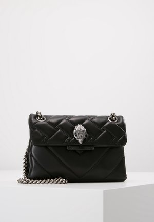 Sac à main en cuir noir matelassé avec bandoulière en chaîne argentée et fermoir argenté en forme de coquillage sur un piédestal blanc.