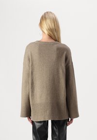 Brun oversized tröja i mjukt stickat material med ribbade ärmslut och fåll. Baksidan har en enkel, sömlös design.