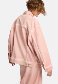 Giacca di jeans rosa con una vestibilità ampia, caratterizzata da un colletto, chiusure a bottoni e un'etichetta a patch sull'orlo. Texture morbida e design minimalista.