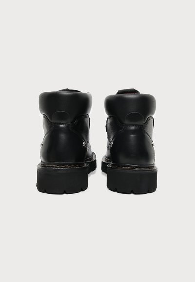 Paire de bottines en cuir noir avec semelles épaisses, vues de dos sur un fond blanc uni.