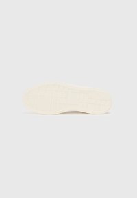 Fehér sneaker talp, textúrázott tapadási mintával és kiemelkedő négyzetekkel. Simán lekerekített él a kerek orrnál. Minimalista dizájn.