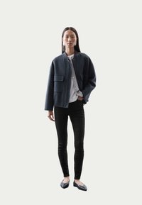 Chaqueta bomber de lana gris oscuro con dos bolsillos frontales, combinada con una camisa gris clara y jeans skinny negros, lleva con bailarinas negras.