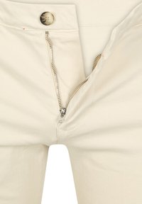 Beige katoenen broeken met een ritssluiting aan de voorkant en een knoopsluiting. De stof is glad met zichtbare stikseldetails langs de naden.