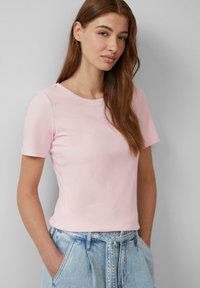 Lichtroze t-shirt met korte mouwen en ronde hals, gemaakt van zacht materiaal. Gecombineerd met lichtblauwe high-waisted denim shorts.