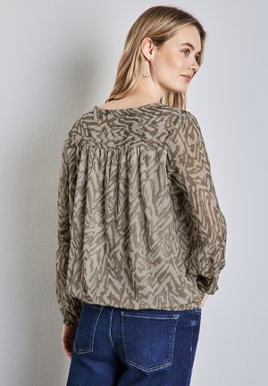 Durchsichtige, leichte Bluse in gedämpftem Oliv mit gestreiftem Muster. Hat einen lockeren Schnitt, einen gerafften Rücken und lange Ärmel. Kombiniert mit dunklen Jeans.