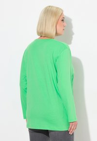 Groen langemouwen t-shirt van jersey stof, met een ronde hals en een ontspannen pasvorm, gecombineerd met donkergrijze broek.