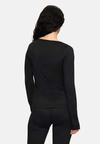 Czarny longsleeve z okrągłym dekoltem, dopasowany fason i miękka tekstura. Posiada zaokrąglony dół oraz detale na bocznych szwach.