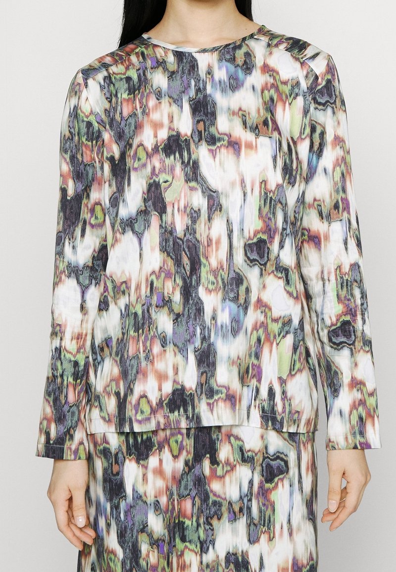 Ensemble haut manches longues et jupe avec un motif abstrait multicolore dans des tons sourds de vert, violet, blanc, noir et marron.