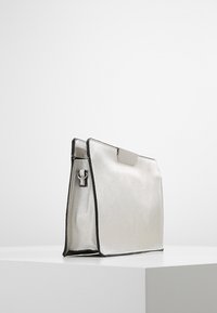 Borsa a mano metallica argento con forma strutturata, bordi neri a contrasto e una chiusura frontale. Presenta un piccolo dettaglio ad anello laterale.