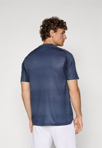 Maglietta sportiva blu navy con un motivo testurizzato, maniche corte e dettagli verdi sul colletto e sulle maniche, vista da dietro.