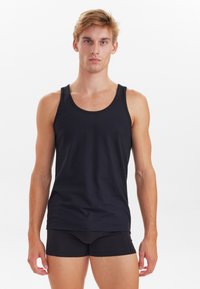Sort bomulds tanktop med en rund halsudskæring og brede skulderstropper, parret med sorte tætsiddende shorts. Glat tekstur, minimalistisk design.