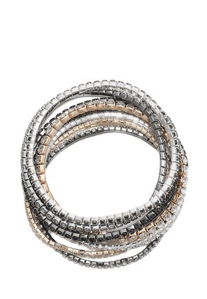 Bracelets flexibles empilés avec des rangées de petits cristaux carrés dans des montures en métal argenté, doré et noir sur fond blanc.