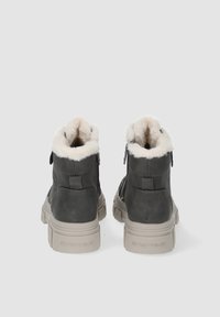 Paire de bottes d'hiver gris foncé avec doublure en fourrure blanche et semelles épaisses beiges, vues de dos sur un fond gris clair.