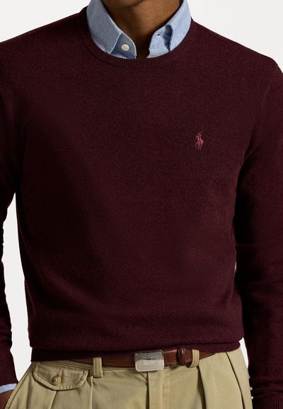 Jersey burdeos de cuello redondo hecho de una tela suave, con un pequeño logo rosa en el pecho, superpuesto a una camisa de color azul claro con cuello.