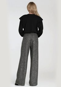 Czarny top z długim rękawem i marszczeniami na ramionach zestawiony z wysokim stanem szerokimi szarymi spodniami o teksturowanym wzorze.