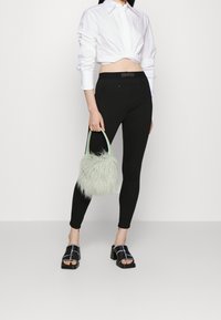 Leggings neri, camicia bianca corta e tacchi neri con tacco spesso. Tiene una borsa fluffy di un verde menta. Design e texture semplici.
