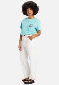Turquoise cotton t-shirt with a palm tree graphic, paired with high-waisted white denim pants and black platform sandals.