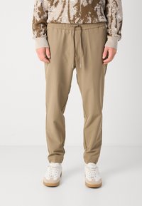 Beige joggerbyxor med elastisk midja och dragsko, med en mjuk textur och smal passform. Kombinerat med vita sneakers.
