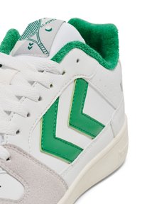 Weißer Sneaker mit grünem Chevron-Design, grün gepolstertem Kragen, grauer Veloursleder-Zehenkappe und weißen Schnürsenkeln.