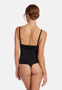 Svart bodysuit med tunna justerbara remmar, sömlös design och en mjuk struktur. Har en låg rygg och höga benöppningar.