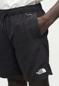 Δεξί χέρι στην τσέπη μαύρου σορτς The North Face με ελαστική μέση και κορδόνι, εμφανίζοντας το κείμενο "FlashDry" κοντά στην τσέπη.