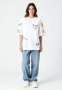 Balta kokvilnas pārspīl�ētā T-krekls ar dažādiem krāsainiem iespiestiem attēliem, tostarp sirdīm, tauriņu un vārdu "mīlestība". Apvienots ar gaiši ziliem džinsiem.