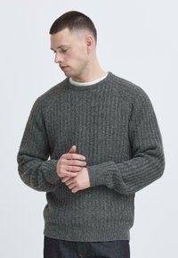 Grå ribbestrikket genser med raglanermer og rund hals. Stoffet har en strukturert overflate og en avslappet passform. Synlige mansjetter og kant.
