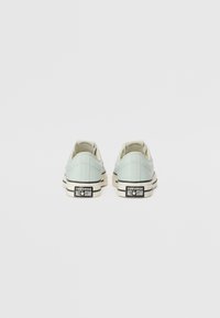Svijetloplave platnene tenisice s crnim i bijelim gumiranim potplatima, s klasičnim niskim dizajnom i "CONVERSE ALL★STAR" markiranjem na peti.