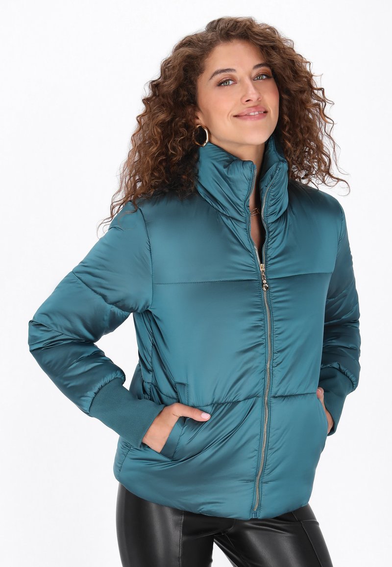 Miękka kurtka puchowa w kolorze teal z wysokim kołnierzem, zamkiem błyskawicznym z przodu i bocznymi kieszeniami. Posiada pikowaną teksturę oraz dzianinowe mankiety dla dodatkowego ciepła.